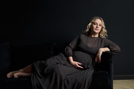Pregnant Woman Posing In An Elegant black Dress indoors studio black wall background Blonde caucasian middle age female six month pregnancy