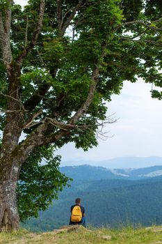 Alone guy sitting on cliff and enjoy peaceful green mountains landscape. Peace of mind and relax.