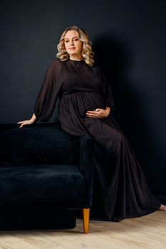 Pregnant Woman Posing In An Elegant black Dress indoors studio black wall background Blonde caucasian middle age female six month pregnancy