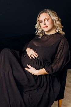 Pregnant Woman Posing In An Elegant black Dress indoors studio black wall background Blonde caucasian middle age female six month pregnancy