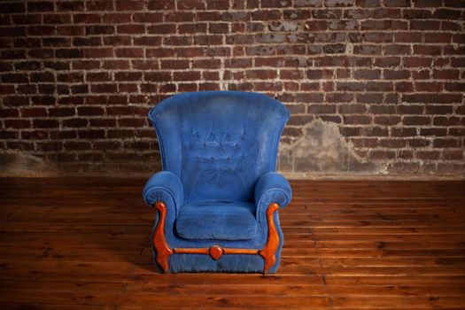 Old dirty vintage blue armchair standing indoor with red brick wall on background