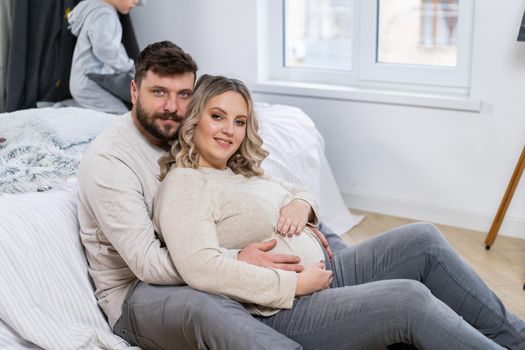 Happy family concept. Husband hug belly pregnant wife sitting floor indoor living room near sofa Caucasian man and woman pregnancy and new life concept. Love and care