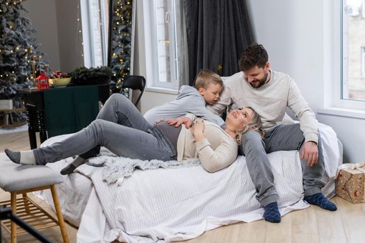 Happy family concept Mother father and little son have fun at home Caucasian family indoors Pregnant mom beard dad and funny little boy lie on the couch