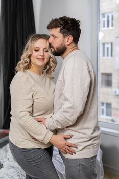 Happy family concept. Husband hug belly pregnant wife standing indoor living room near sofa Caucasian man and woman pregnancy and new life concept. Love and care