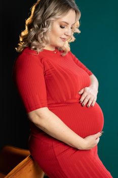 Pregnant Woman Posing In An Elegant red Dress indoors studio green wall background Blonde caucasian middle age female six month pregnancy