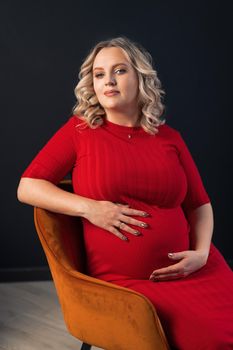 Pregnant Woman Posing In An Elegant red Dress indoors studio black wall background Blonde caucasian middle age female six month pregnancy