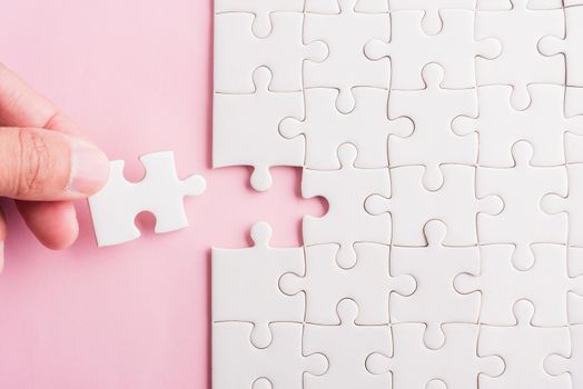 Top view flat lay of hand-holding last piece white paper jigsaw puzzle game last pieces put to place for solve problem complete mission, studio shot on a pink background, quiz calculation concept