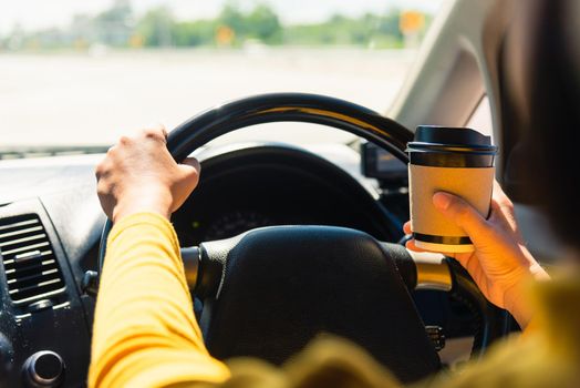 Asian woman drinking hot coffee takeaway cup inside a car and while driving the car in the morning during going to work on highway, Transportation and vehicle concept