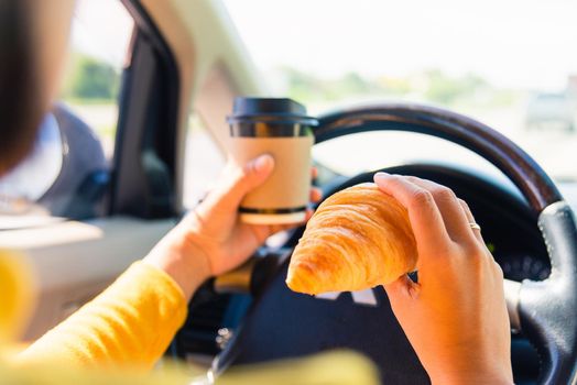 Asian woman eating food fastfood and drink coffee while driving the car in the morning during going to work on highway road, Transportation and vehicle concept