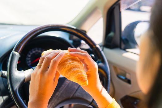 Asian woman eating food fastfood while driving the car in the morning during going to work on highway road, Transportation and vehicle concept