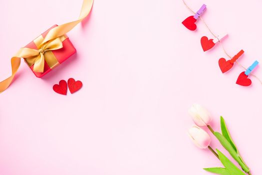 Happy Valentine's day composition background concept. Red gift box with a golden bow ribbon and wood red hearts for love isolated on pink background with copy space. Top View from above