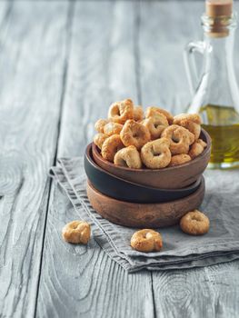 Traditional italian snack taralli or tarallini in wooden bowl over old gray wooden table. Rustic shot of taralli appetizer with copy space. Vertical.