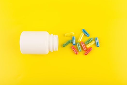 Flat lay with white medication bottle with spilled multicolored pills against yellow background. Concept of vitamins for kids or pharmacy and healthcare