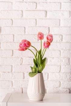 White vase with bouquet of pink tulips on brick wall background
