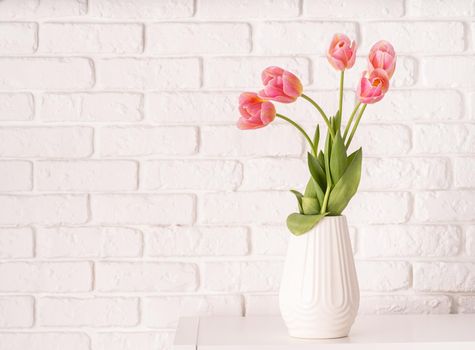 White vase with bouquet of pink tulips on brick wall background with copy space