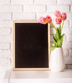 Easter hliday concept. Vase with tulips and black felt letter board with words Happy Easter on white bricks background