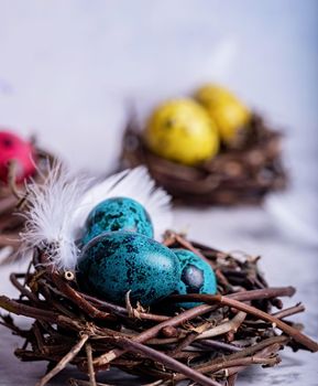 Easter holiday concept. Colored Easter quail eggs in a nest on gray marble background