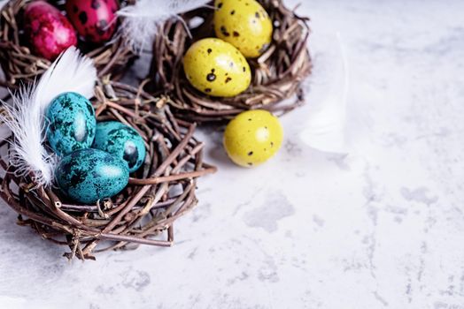 Easter holiday concept. Colored Easter quail eggs with feathers in a nest on gray marble background with copy space