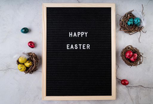 Easter holiday concept. The words Happy Easter on black felt letter board decorated with quail eggs and feathers on marble background