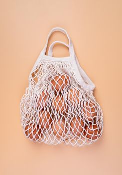Easter concept. No plastic bag concept. Minimal concept. White mesh shopping bag with brown chicken eggs on beige background top view flat lay
