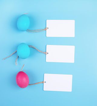 Easter concept. Colored eggs with blank tags isolated on blue background top view