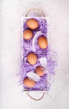 Easter holiday concept. White wooden box with chicken eggs on white marble background top view flat lay