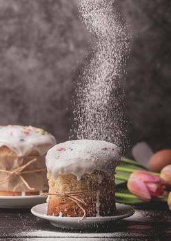 Easter concept. Baking and cooking. Sugar powder falling on glazed easter cake on dark rustic background