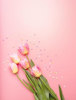 Pink and yellow tulips decorated with small hearts on pink background flat lay top view with copy space