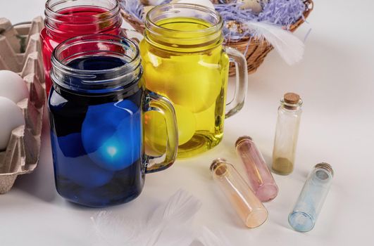 Easter holiday concept. Eggs coloring. Three mason jars with colorful eggs inside on the table front view