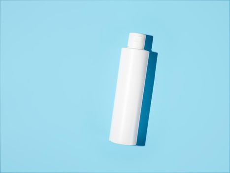 Empty white plastic bottle mockup in hard light. Top view or flat lay. Blank opaque bottle without packaging on blue background. Mock up for package design