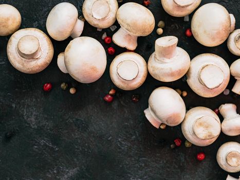 Mini champignons with copy space on left edge. Raw whole mushrooms on black background, copy space. Top view or flat lay.