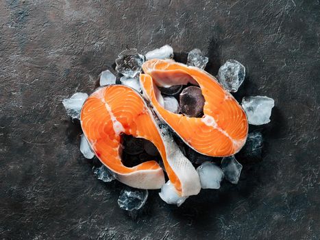 Two raw wild salmon steaks on ice over black textured background. Salmon steaks top view or flat lay.