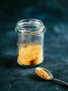 Indian or pakistani masala powder in spoon and glass jar. Homemade dry curry garam masala mix spices blend on dark gray and blue background. Vertical