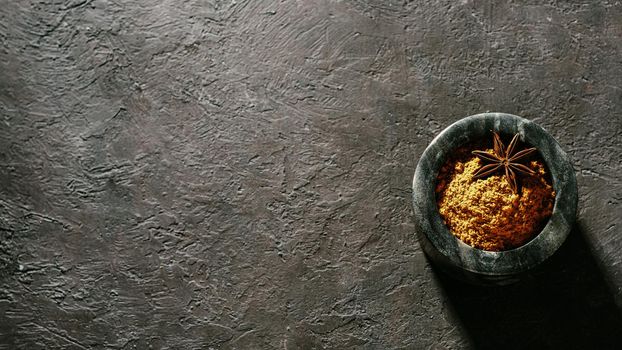 Indian or pakistani masala powder in black marble bowl on black textured background. Small marble bowl with dry curry garam masala mix spices blend with copy space. Top view or flat lay.