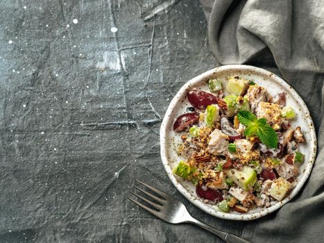 Waldorf salad with copy space. American fruit and nut salad with apples, celery, grapes, chicken meat, dressed mayonnaise. Craft plate with ready-to-eat waldorf salad on gray background. Top view