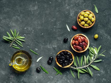Set of green, black and red or pink olives and olive oil on dark background. Different types of olives in olive wooden bowls and olive oil over dark canvas background. Copy space. Top view or flat lay