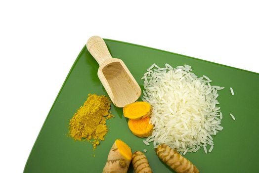 Fresh raw turmeric roots and slices next to heaps of rice and spice powder on a green plate with free space for text