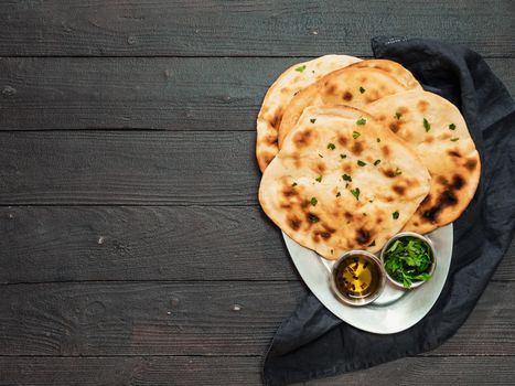 Fresh naan bread on dark wooden background with copy space. Several perfect naan flatbreads over metal tray. Top view or flat lay.