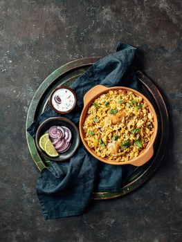 Pakistani food - biryani rice with chicken and raita yoghurt dip. Delicious hyberabadi chicken biryani over tray on black background. Top view or flat lay. Vertical.