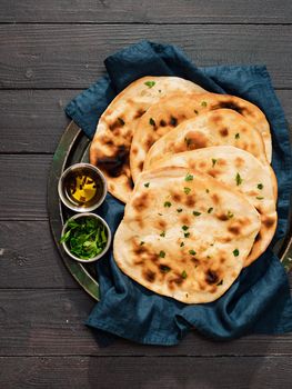 Fresh naan bread on dark wooden background with copy space. Several perfect naan flatbreads on blue linen napkin. Vertical. Top view or flat lay.