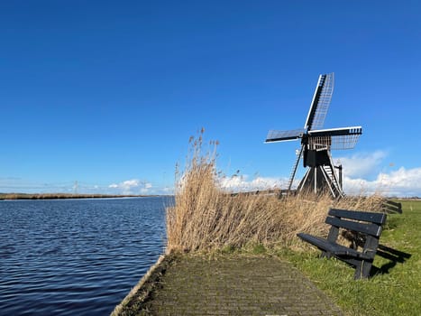 Park bench next to a windmill and a canal around Akkrum in Friesland The Netherlands