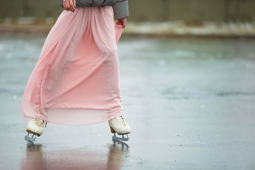 Close-up of female legs on white figure skates in winter at an outdoor ice rink.