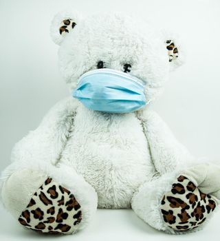 Masked teddy bear with surgical mask on white background