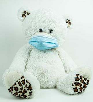 Masked teddy bear with surgical mask on white background