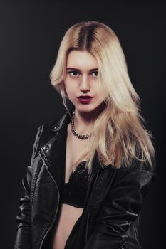 A beautiful, glamour young blond Girl in a black jacket is posing on black background