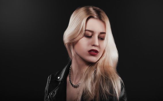 A beautiful, glamour young blond Girl in a black jacket is posing on black background