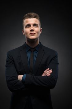 a portrait of a handsome young businessman is thinking and looking up against a black background. success concept