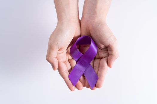 World cancer day, hands holding purple ribbon on grey background with copy space for text. Healthcare and medical concept.