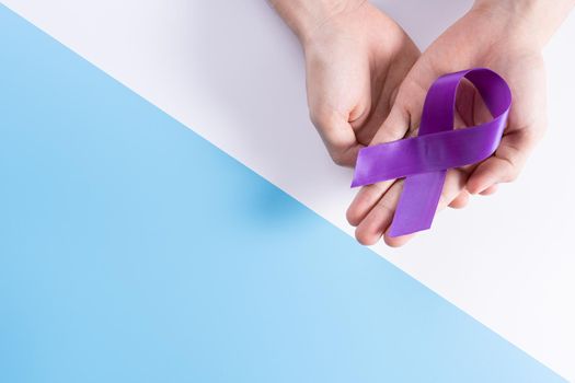 World cancer day, hands holding purple ribbon on with and blue background with copy space for text. Healthcare and medical concept.