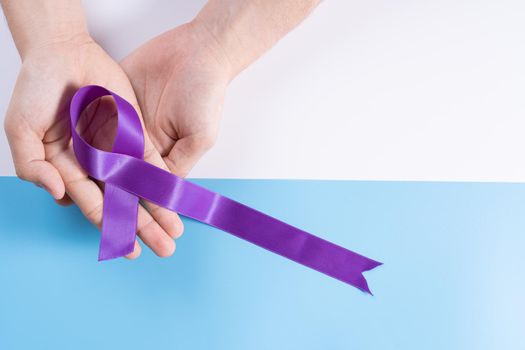 World cancer day, hands holding purple ribbon on with and blue background with copy space for text. Healthcare and medical concept.